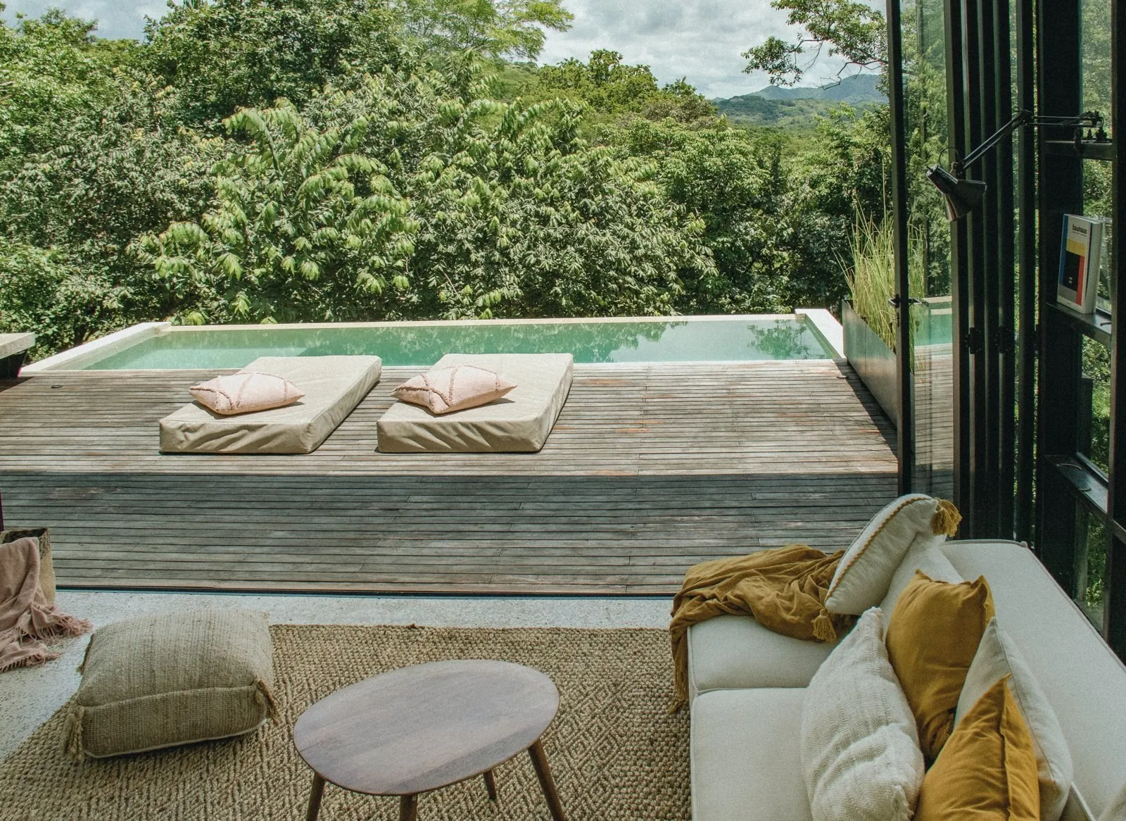From the sofa inside: the open deck with two pink cushions, the pool and the canopy, hills in the distance.